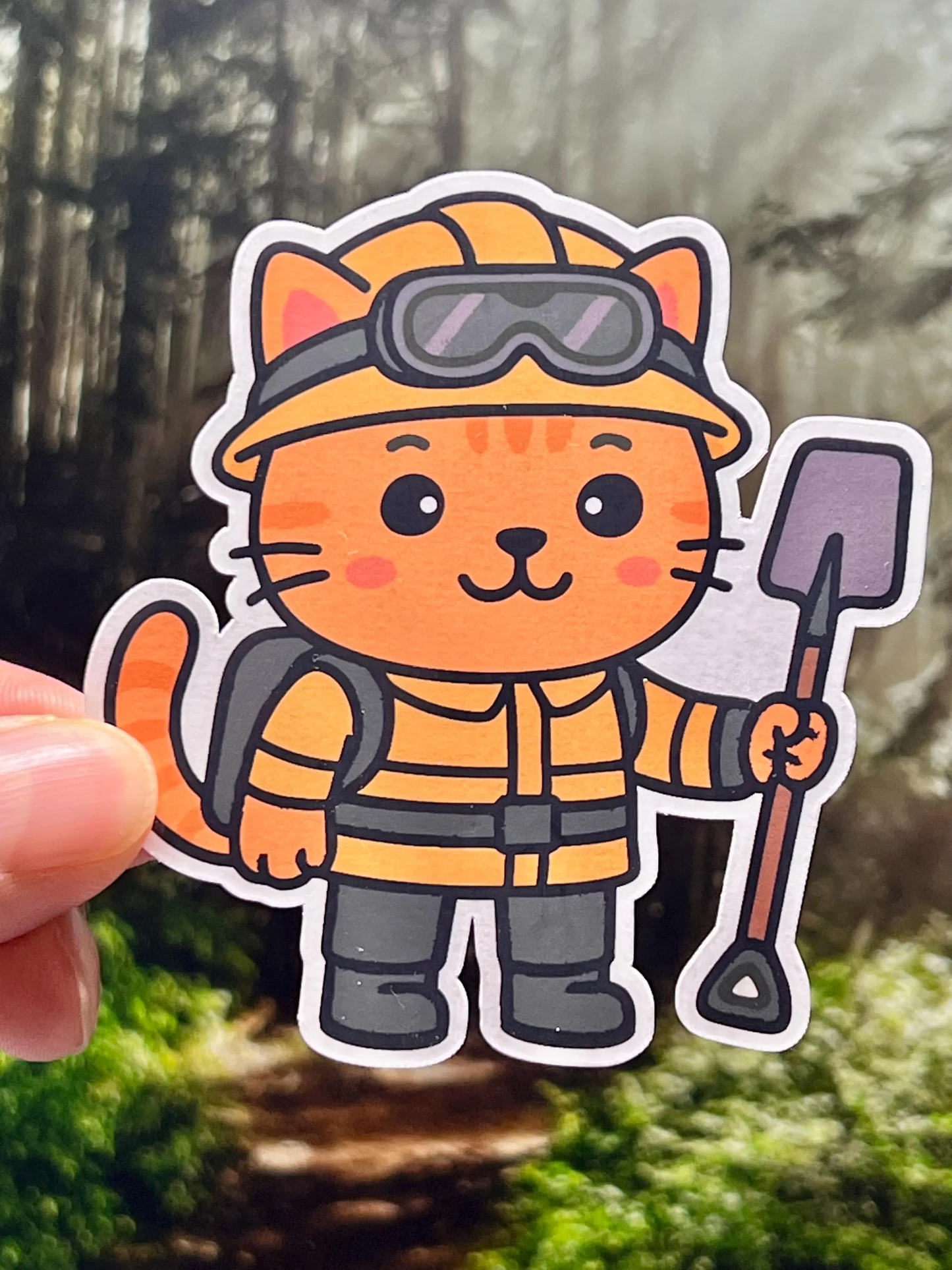 Sticker of woodland firefighter cat in a firefighting gear holding a shovel