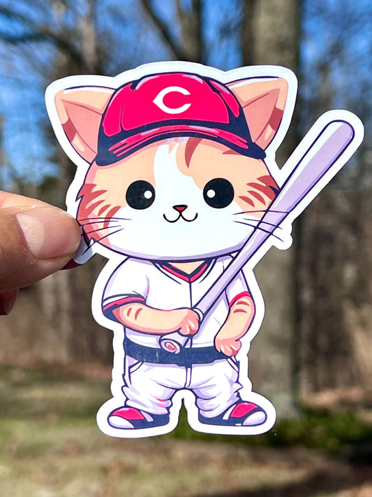 A sticker of a cartoon cat wearing a Cincinnati Reds baseball uniform, holding a baseball bat.