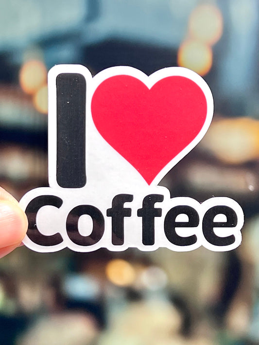 A vinyl sticker with the text 'I LOVE COFFEE' and a heart symbol replacing the word 'LOVE'. The sticker is red with a black outline and a white background.