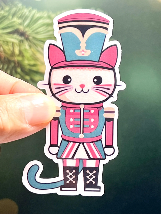 A sticker of a cute cat dressed as a nutcracker soldier in a colorful outfit.