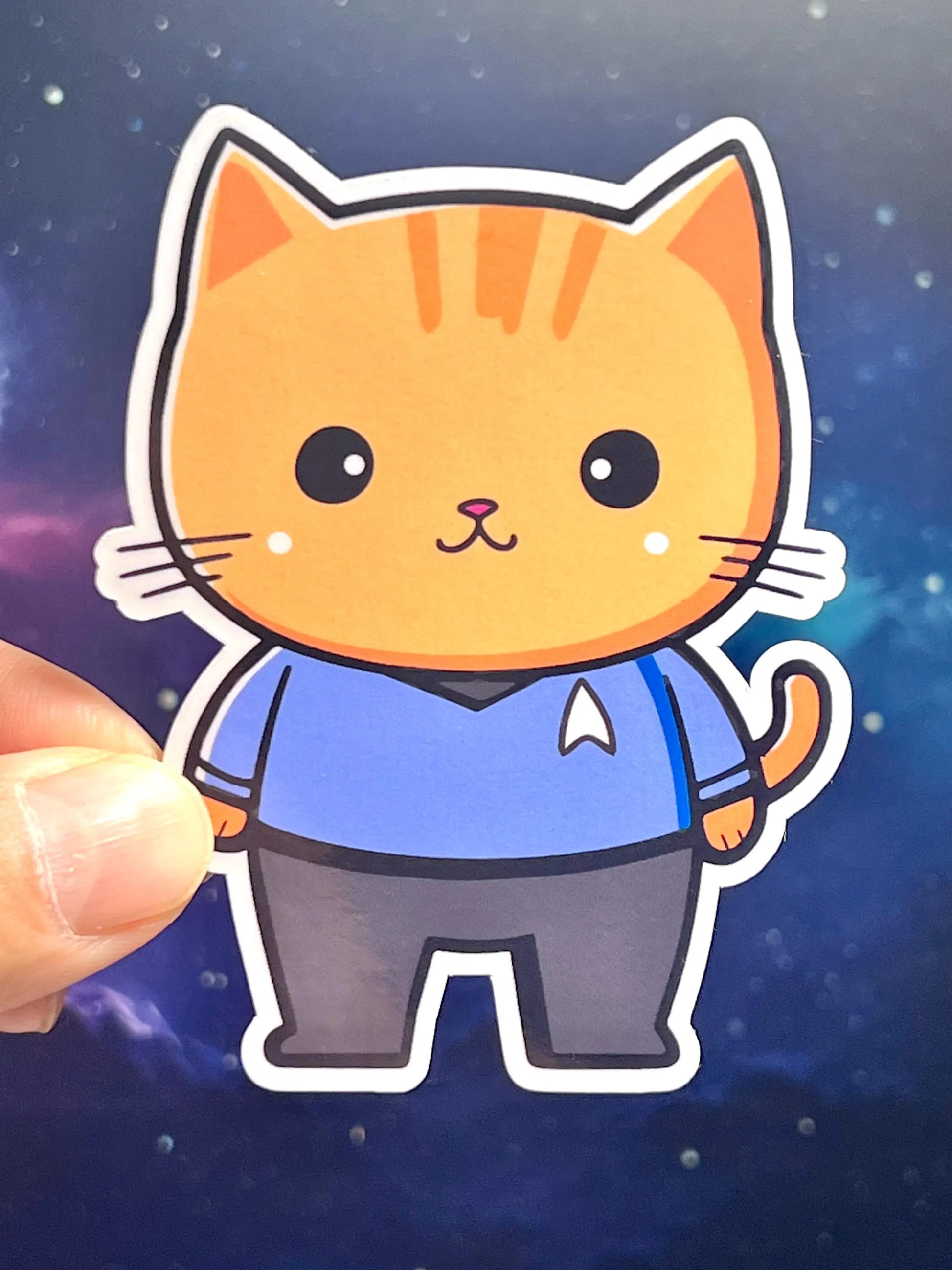A sticker of a cartoon cat wearing a blue Star Trek uniform and black pants