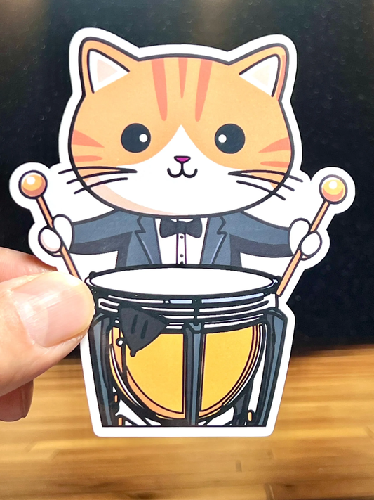 A vinyl sticker of a cartoon cat timpani player holding two mallets and standing behind a timpani